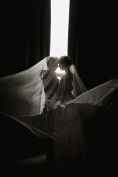 a bride and groom kissing in front of a window with the veil blowing over them