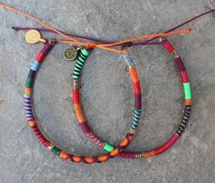 three bracelets with different colored beads are on the ground and one has a gold disc