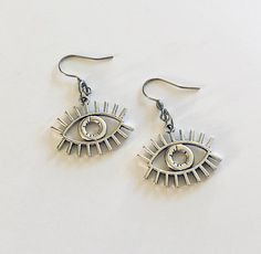 Evil eye earrings, silver eye earrings, ancient Egyptian/ Greek protection from the evil eye earrings, detailed eye charms. STAINLESS STEEL ear wires fish hooks jewelry. Egypt god Horus, for that witchy woman, Wicca Wiccan Witch. Occult esoteric occultism *earring wires measure approx .6 of an inch, or just over half an inch *charm itself approx .8 of an inch, (or just over half an inch) *STAINLESS STEEL earring wires fish hooks *charms are silver alloy *comes in a gift box earrings eye evileye Eye Themed Clothes, Metal Dangle Earrings With Evil Eye, Symbolic Eye-shaped Silver Jewelry, Silver Dangle Jewelry With Diamond Eyes, Occult Jewelry, Wiccan Earrings, Fish Hook Jewelry, God Horus, Witchy Earrings