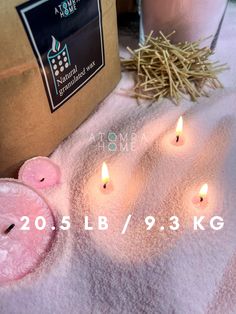 some candles are sitting on a towel next to a box with straw in it and another candle is lit