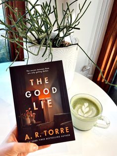 a person holding up a book on top of a table next to a cup of coffee