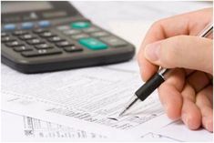 a person holding a pen while sitting at a desk next to a calculator