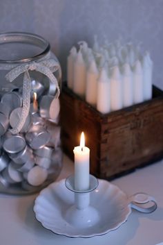 a candle is sitting on a plate next to a glass jar filled with white candles