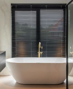 a white bath tub sitting next to a window covered in blinds