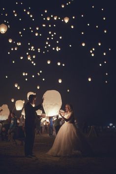 a bride and groom standing in front of paper lanterns flying above the ground at night