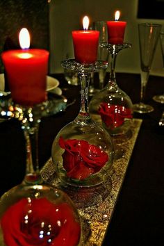 wine glasses with red roses in them are sitting on a table next to some candles