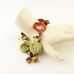 "This distinctive new lampwork bracelet is designed with my handmade lampwork beads in a pretty sage green with swirls of blue, and splashes of brown, gold, cream, and more. I have combined the glass beads with a unique copper connector that has raised brass studs, antique brass and copper beads, and Swarovski crystals. This one of a kind bracelet is finished with a copper toggle clasp that coordinates with the copper component in the bracelet. Lots of movement and fun in this new bracelet! This Artisan Green Bracelets With Spacer Beads, Artisan Green Bracelets For Jewelry Making, Green Czech Glass Beaded Bracelets, Green Beaded Bracelets With Natural Stones, Unique Green Beaded Bracelets With Natural Stones, Lampwork Bracelets, Artisan Bracelets, Handmade Lampwork Bead, Green Garnet