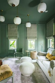 a living room with green walls and white furniture in the center, along with two large round foot stools