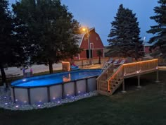 an above ground swimming pool surrounded by trees and decking with lights on the sides