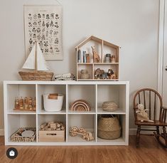 a white shelf filled with lots of toys on top of a hard wood floor next to a wooden rocking chair