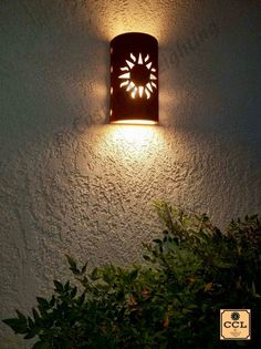 a light that is on the side of a wall next to some plants and bushes