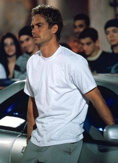 a man standing in front of a group of people next to a blue sports car