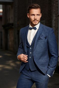 a man in a blue suit and bow tie posing for the camera with his hands on his hips