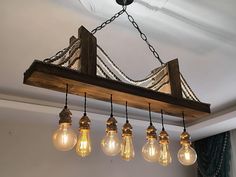 a wooden beam with five light bulbs hanging from it's sides and an iron chain on the end