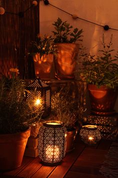 several lit candles sitting on top of a wooden table next to potted planters