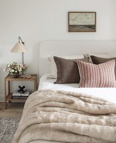 a bed with pillows and blankets on top of it next to a nightstand in a bedroom