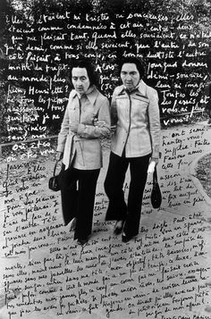 two women standing next to each other in front of a wall with writing on it