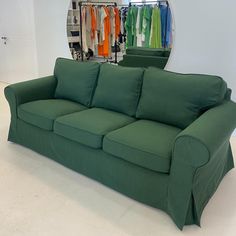 a green couch sitting in front of a mirror with clothes hanging on the rack behind it