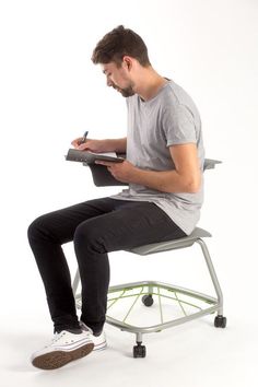 a man sitting on a chair with a laptop and pen in his hand while he is writing