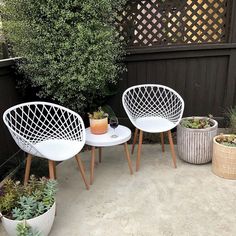 three white chairs sitting next to each other on top of a cement floor near plants