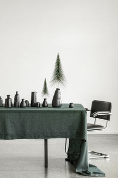 the table is covered with green cloth and silver vases next to a pine tree