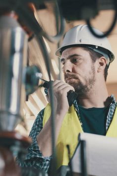 a man wearing a hard hat and holding a cell phone to his ear while standing next to machinery