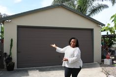 a woman standing in front of a garage with her hand out to the side and palm trees behind her