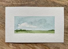 a watercolor painting of a green field with clouds in the sky on top of it