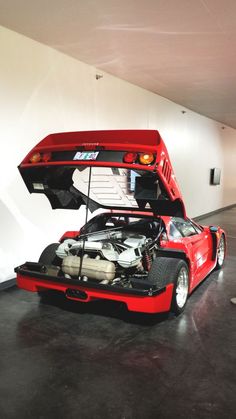 a red sports car with its hood open in a parking garage next to a white wall