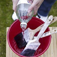 a person pouring something into a bucket with paintbrushes and spatulas in it