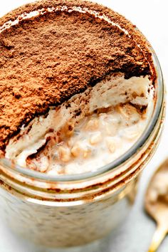 a glass jar filled with pudding and ice cream on top of a white surface next to a spoon