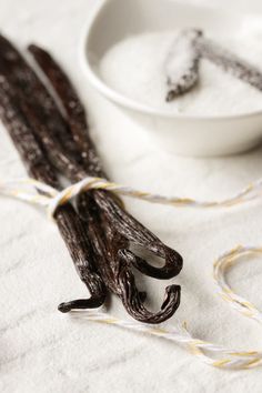 two sticks of vanilla are tied up next to a bowl of sugar and twine