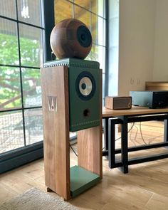 a speaker sitting on top of a wooden block in front of a table with a large window