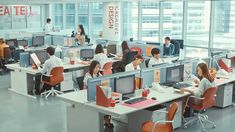 an office filled with people working on computers and sitting at desks in front of large windows