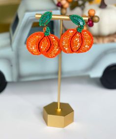 an orange beaded pair of earrings sits on a stand in front of a toy truck