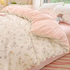 a bed with pink comforter and pillows in a room next to a window,