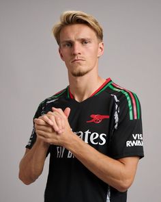 a young man in a black jersey holding his hands together and looking at the camera