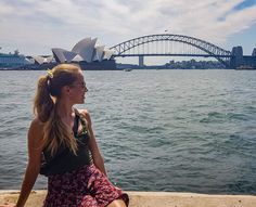 a woman sitting on the edge of a pier next to water