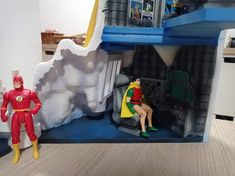 two figurines sitting in front of a toy house with a man and woman inside