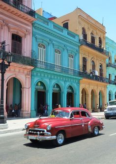 an old red car is parked in front of colorful buildings