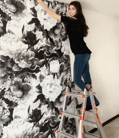 a woman on a ladder painting a flowered wall with black and white florals