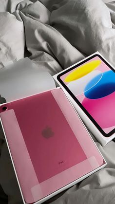 two different colored ipads sitting on top of a white bed next to each other