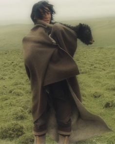 a man in a brown cape standing on top of a lush green field