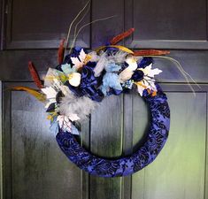 a blue wreath with feathers and flowers hanging on a door