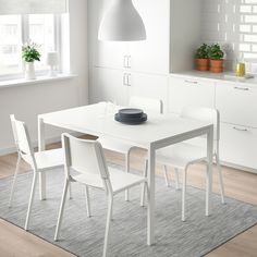 a white dining table with four chairs and a bowl on the table in front of it