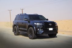 a black suv driving down the road in the desert