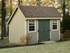 a small shed with a brown roof and green doors in the grass next to trees