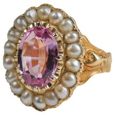 An unapologetically regal natural, untreated pink topaz gemstone is surrounded by a halo of natural uncultured saltwater pearls in this magnificently rare and beautiful unisex ring from the second half of the 19th century. Dating to 1843 and made in London, this 18K yellow gold ring features one of the rarest gemstones in the world: natural pink topaz. Not to be confused with 99% of the pink topaz you may have encountered, which —like blue topaz— owes its color to irradiation. This spectacular pink gem has had no treatment whatsoever. The gem is beautifully cut with tremendous fire. This 12w.5mm x 8.7mm weighs 4 carats and resides within numerous secure hand-carved prongs, surrounded by 18 small, fine natural saltwater pearls. Ornately hand-engraved shoulders lead around to the rear and a Imperial Topaz Ring, Wear Pearls, Imperial Topaz, Pink Gem, Topaz Necklace, Pink Topaz, Rare Gemstones, Unisex Ring, Pink Gemstones