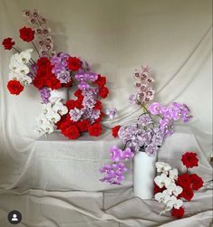 three white vases filled with red, purple and white flowers on top of a bed