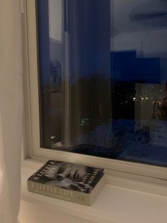 a book sitting on top of a window sill in front of a white curtain